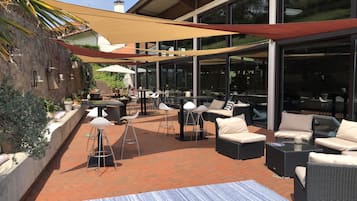Une terrasse extérieure aménagée avec des meubles en osier, un tapis à rayures et un grand parasol offrant de l’ombre.
