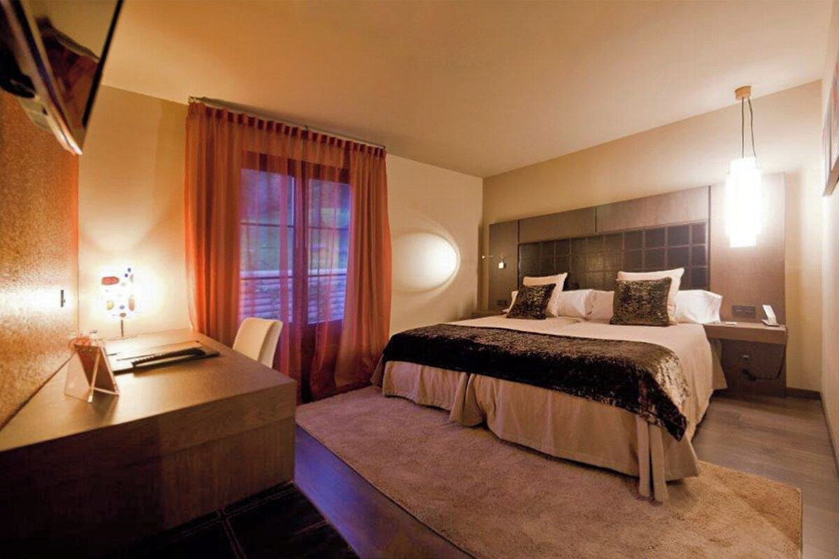 A hotel room with a bed, bedside table, lamp, and curtains.