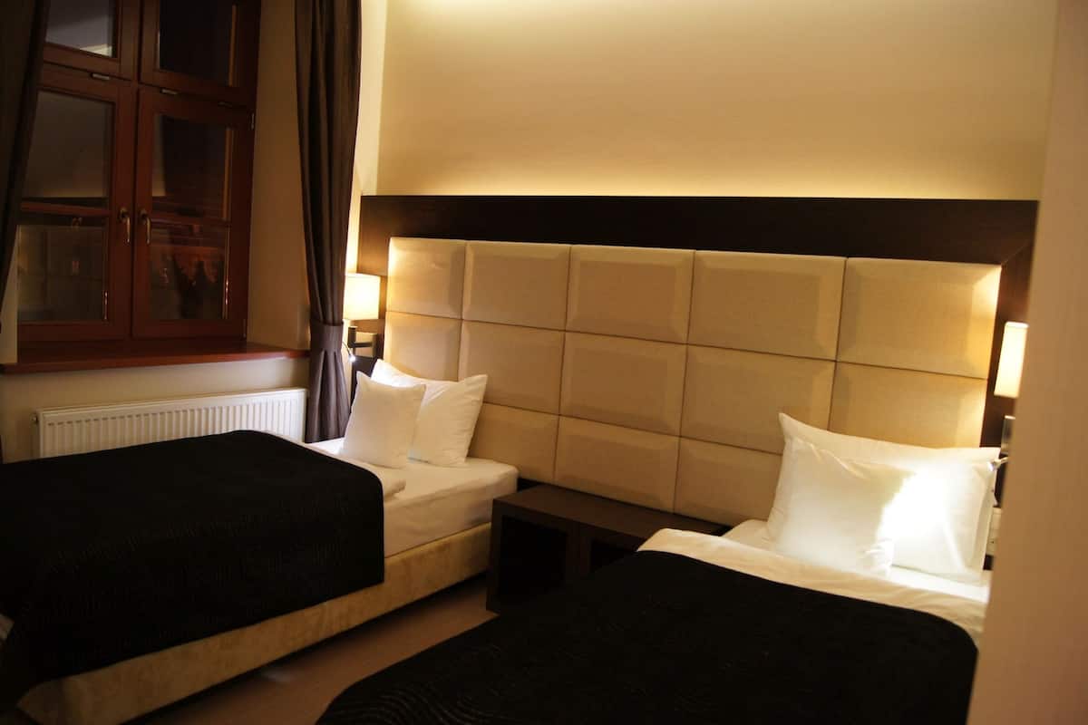 A hotel room with two beds, a wooden cabinet, and a radiator.