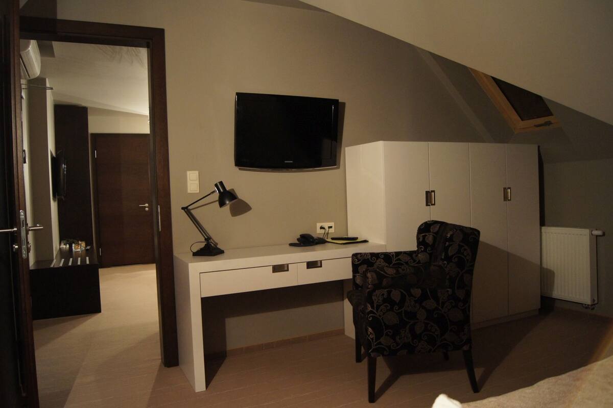 A bedroom with a desk, chair, TV, wardrobe, and a sloped ceiling.