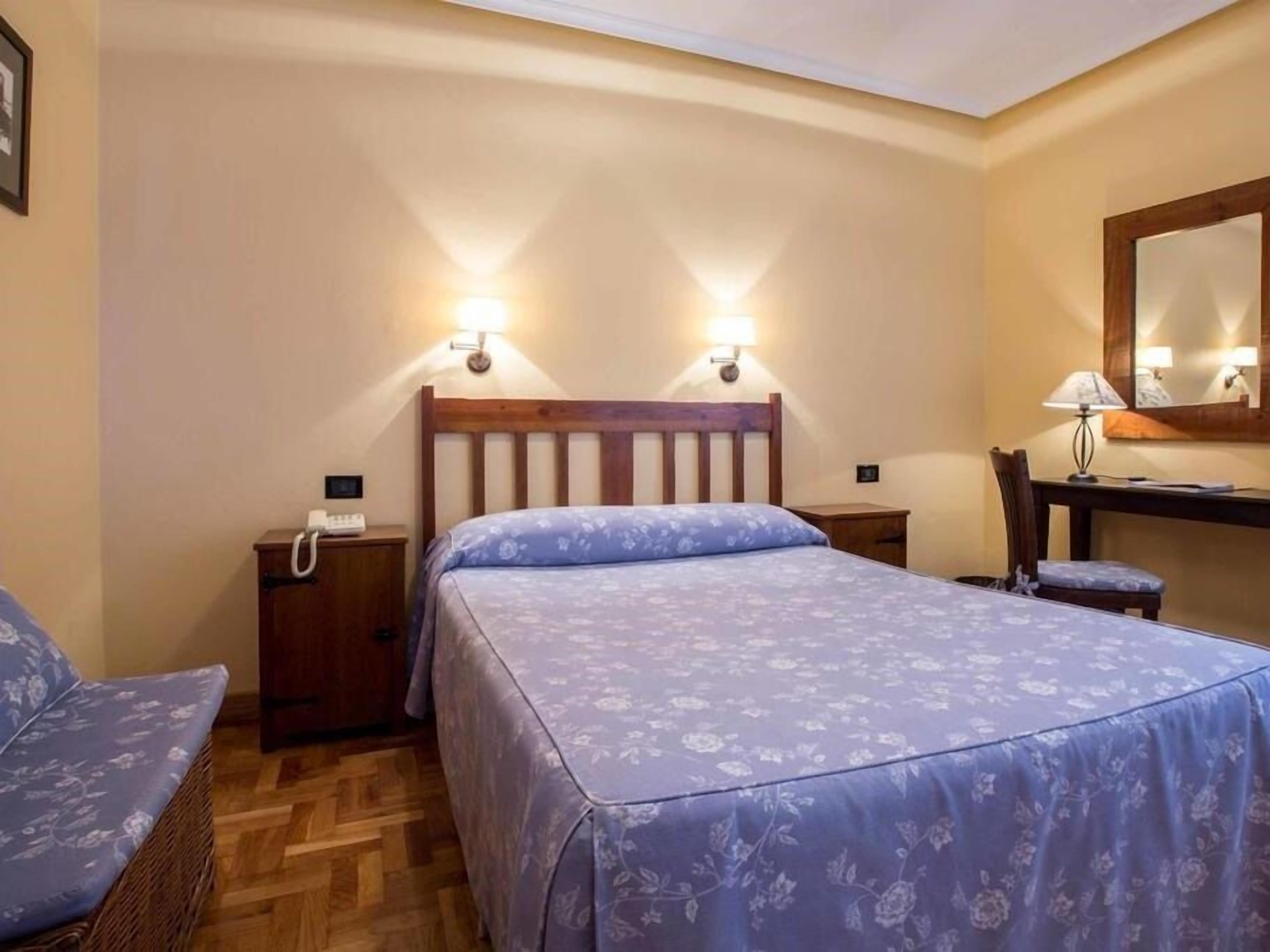 Un dormitorio con cama, una silla, un escritorio y una mesita de noche.