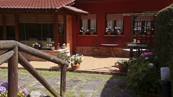 Un edificio rojo con tejado de tejas, zona de recepción y mesas al aire libre.