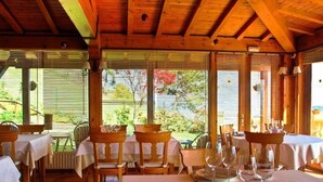 Un restaurante con vigas de madera, mesas dispuestas para comer y grandes ventanales con vistas a un jardín.