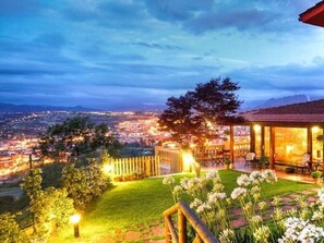 A view of a cityscape at dusk with a well-lit outdoor seating area and a garden with flowers. - Hotel Casa Camila (Oviedo)