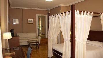 Une chambre d’hôtel dotée d’un lit à baldaquin, d’un coin salon avec un canapé et une table, ainsi que d’un coin repas avec une table et des chaises.