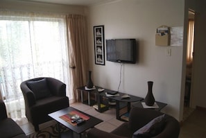 Uma sala de estar com sofá, mesa de centro, televisão e um vaso.