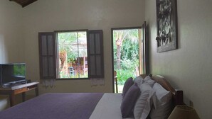 A bedroom with a bed, a desk with a computer, two windows, and a painting on the wall. - Pousada da Terra Paraty (Paraty)
