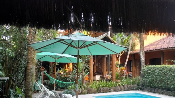 A poolside area with lounge chairs and umbrellas, a pool, and a thatched roof structure. - Pousada da Terra Paraty (Paraty)