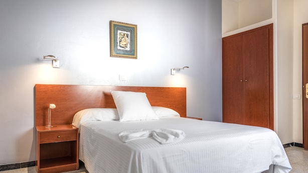 A neatly made bed with white linens, a wooden headboard, and two bedside tables with lamps. - Hotel Blanca Paloma (Las Palmas de Gran Canaria)