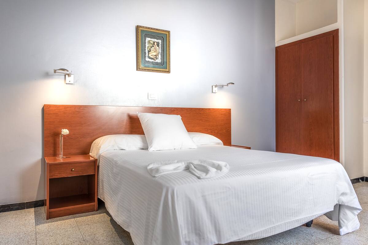 A neatly made bed with white linens, a wooden headboard, and two bedside tables with lamps.