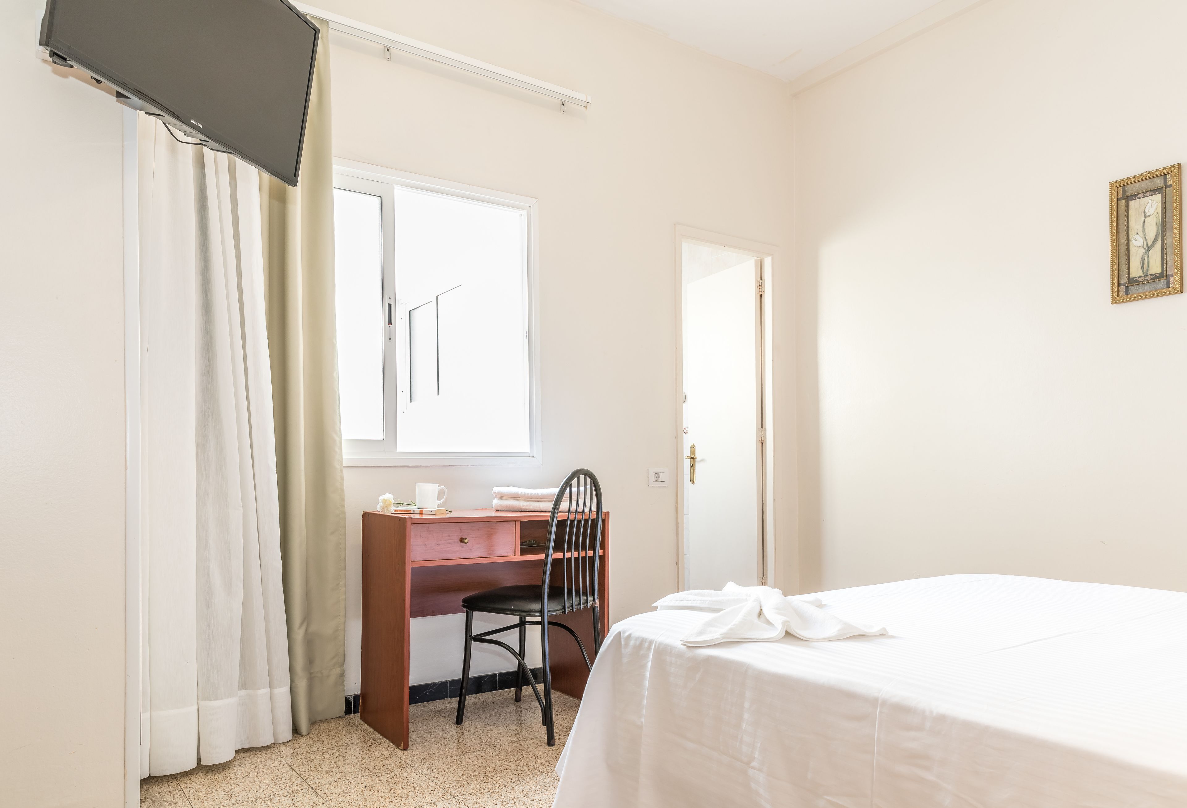 A bedroom with a bed, a desk, a chair, a window, and a door.