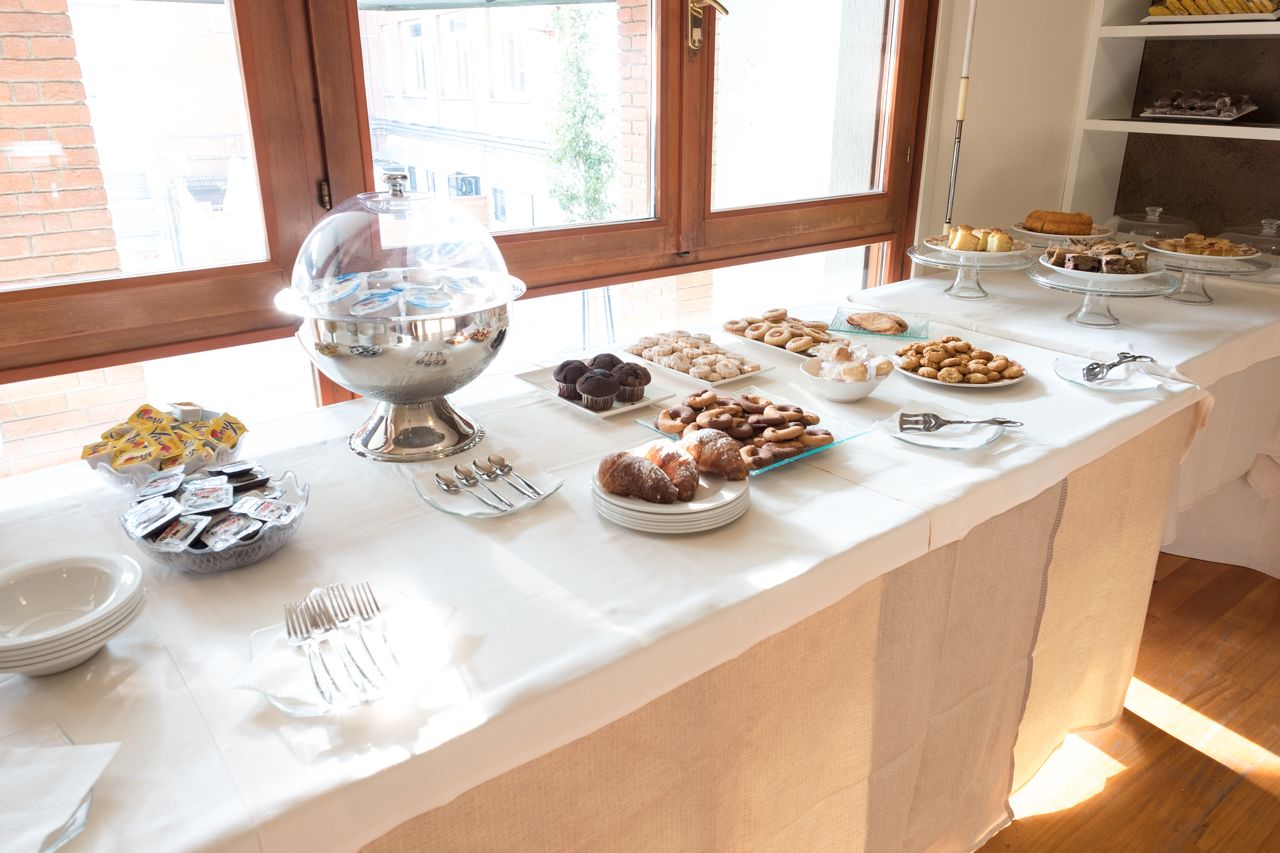 A buffet table with various pastries and a large bowl of food, set against a window with a view of buildings.