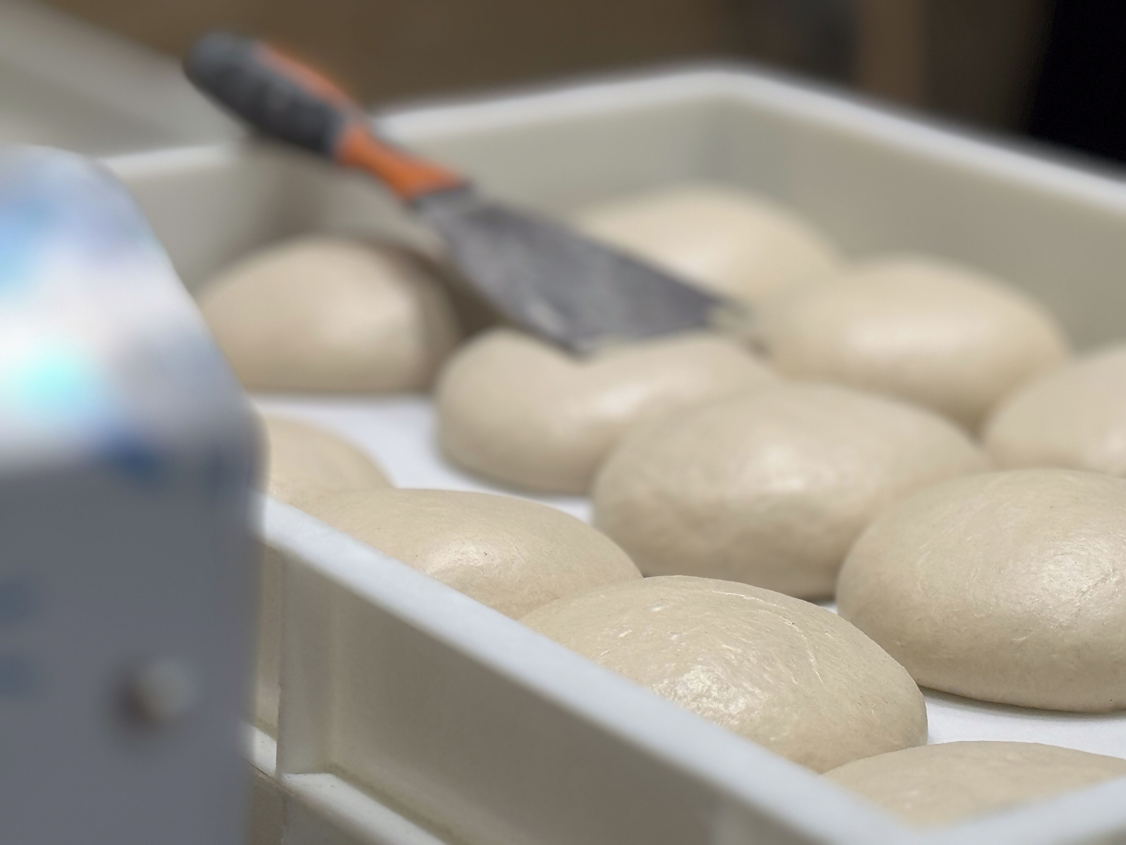 A tray of round, unbaked dough balls with a dough scraper in the background.