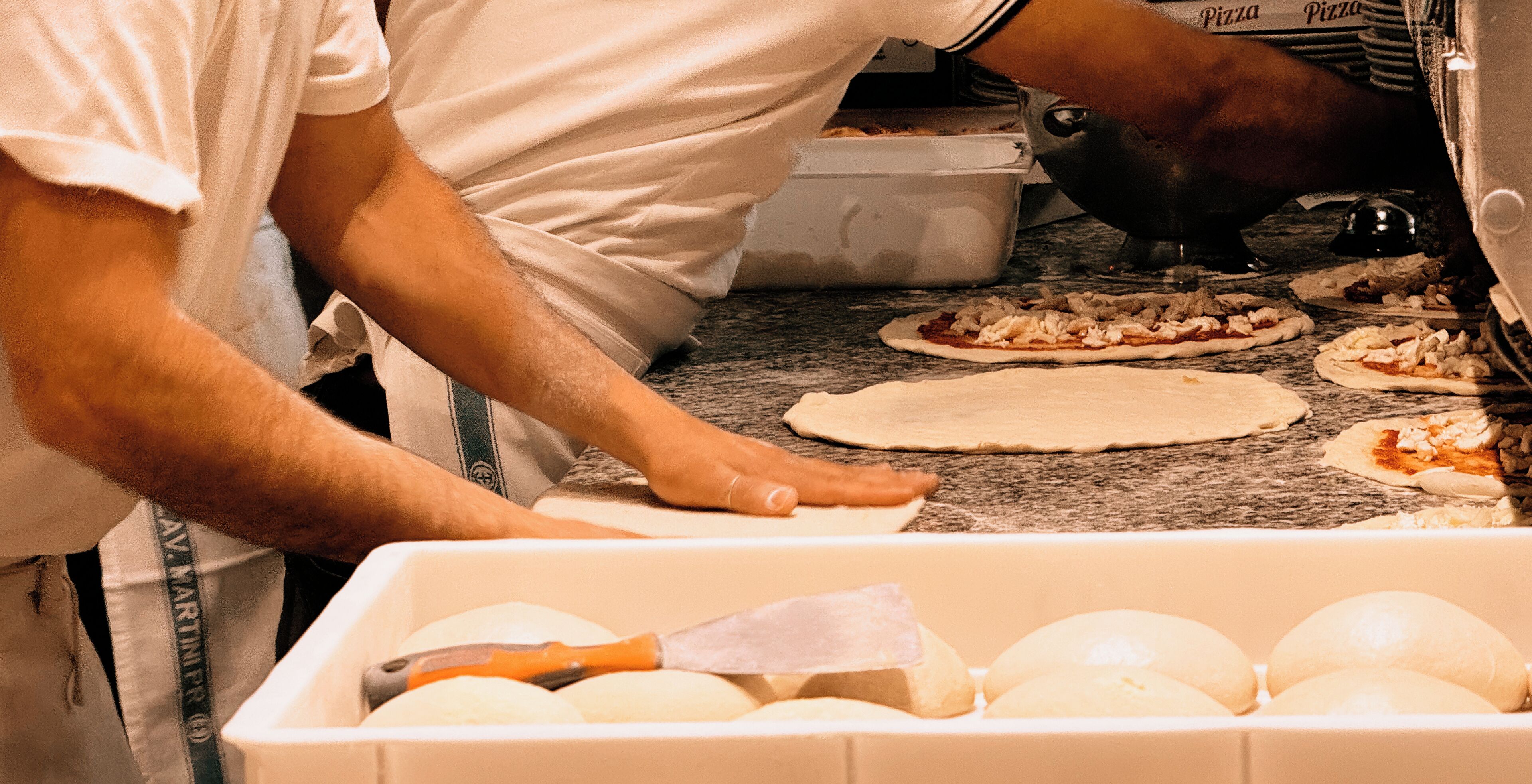 A kitchen with a person preparing pizza dough.