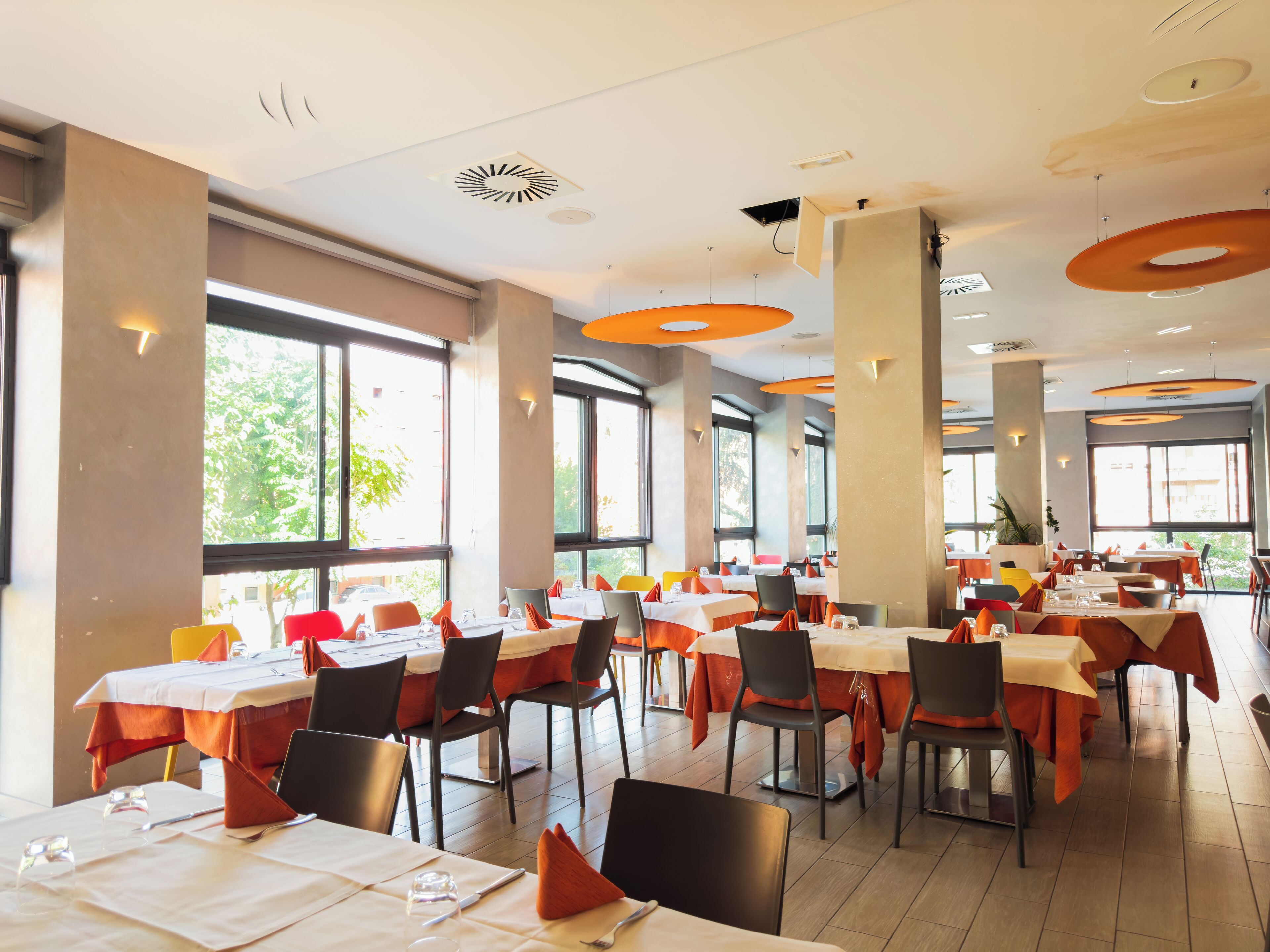 A spacious restaurant with multiple tables and chairs, large windows, and modern ceiling design.