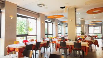 A spacious restaurant with multiple tables and chairs, large windows, and modern ceiling design.