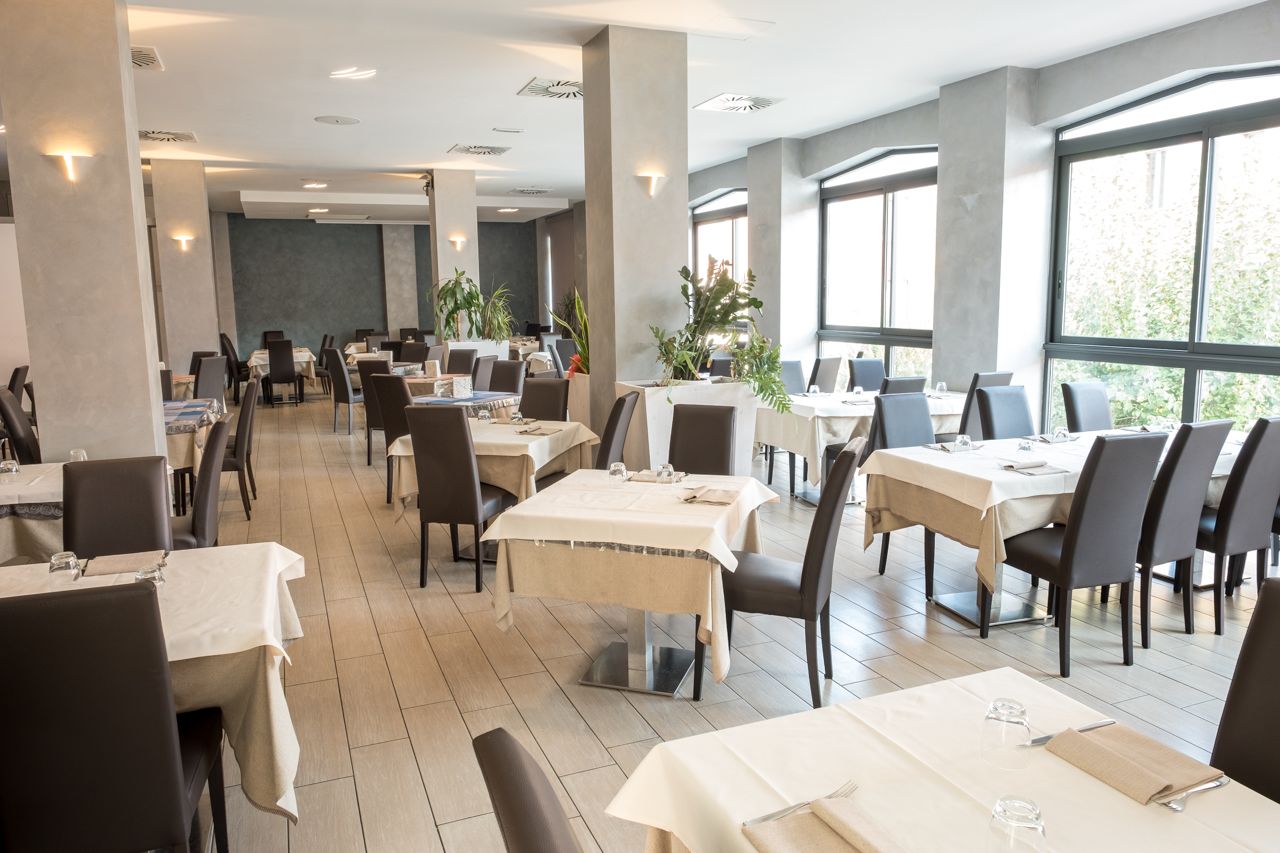 Un comedor espacioso con varias mesas y sillas, ventanas amplias y plantas de interior.