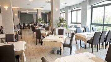 Un comedor espacioso con varias mesas y sillas, ventanas amplias y plantas de interior.