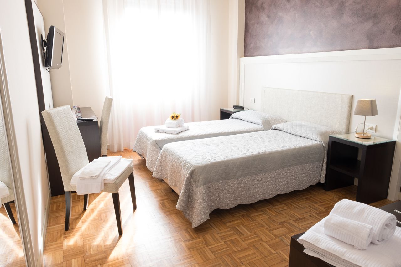 A hotel room with two beds, a desk, a chair, and a TV.