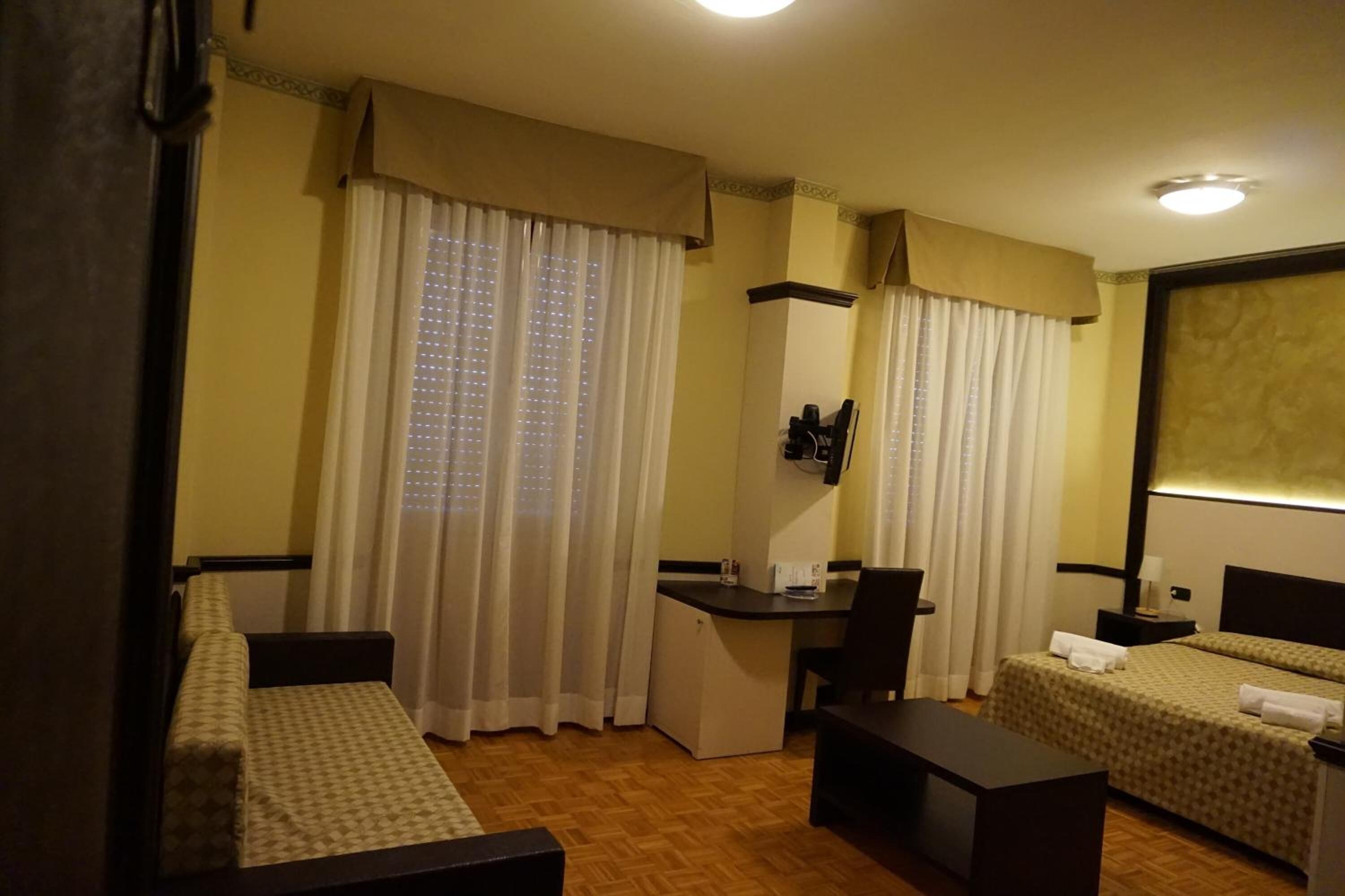 Habitación de hotel con dos camas individuales, un escritorio, una silla, un refrigerador pequeño y un espejo.