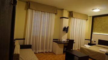 Habitación de hotel con dos camas individuales, un escritorio, una silla, un refrigerador pequeño y un espejo.
