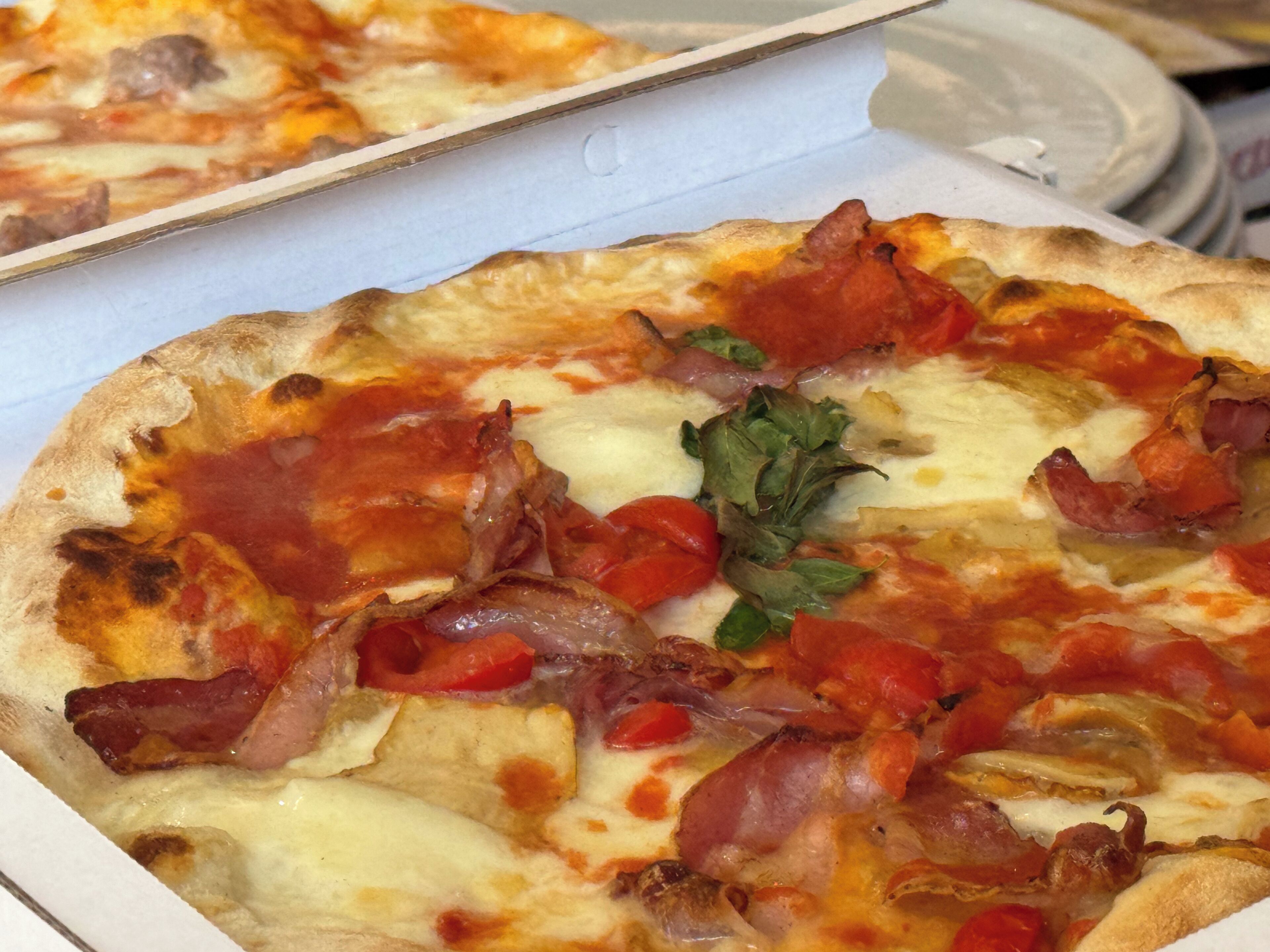 Eine Pizza mit Belag aus Speck, Käse und Tomaten.
