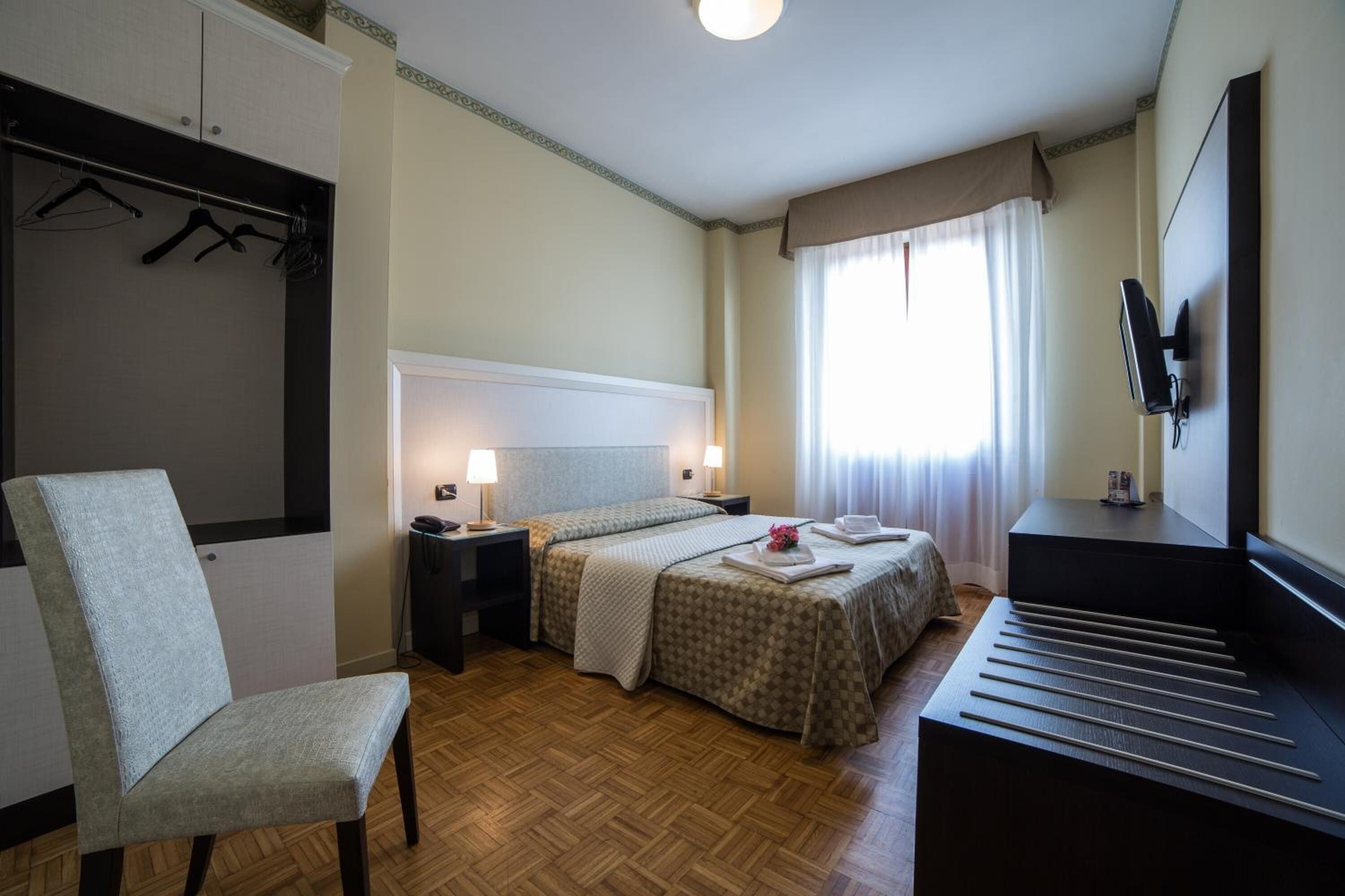Una habitación de hotel con una cama, una silla, un escritorio, un televisor y un armario.