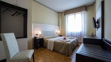 Una habitación de hotel con una cama, una silla, un escritorio, un televisor y un armario.