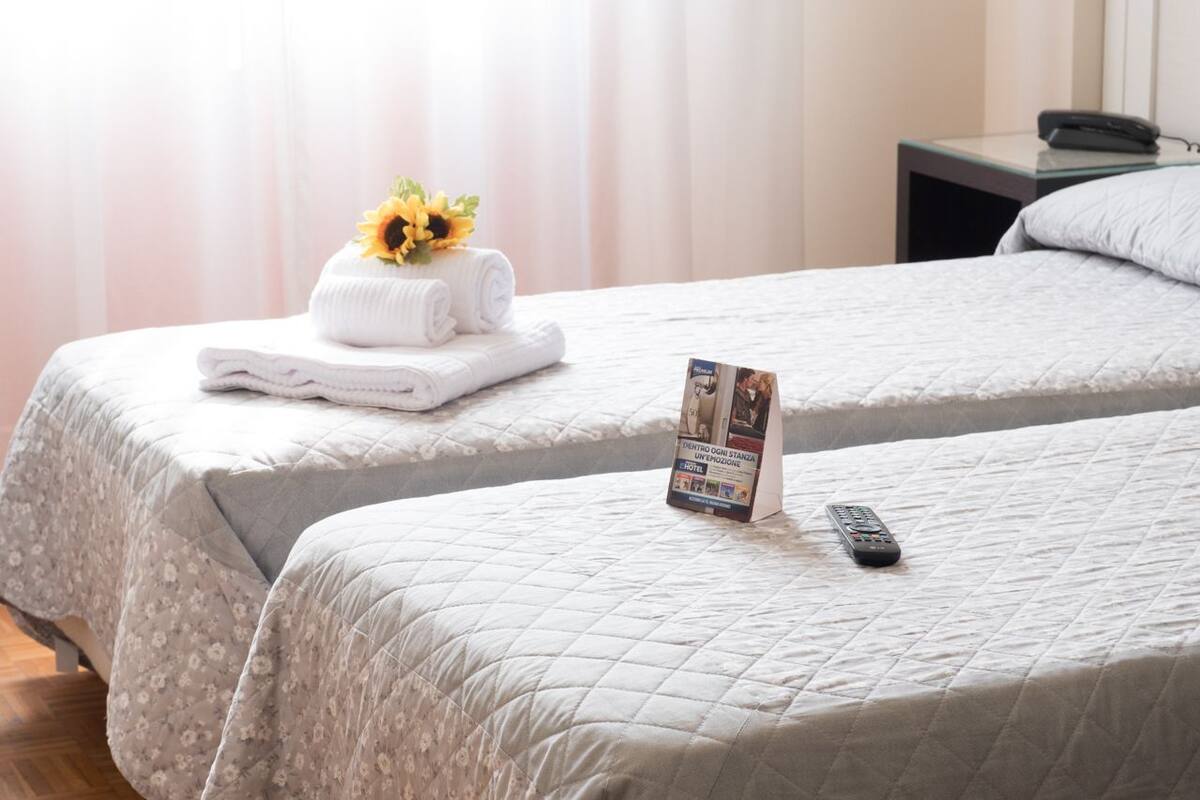 A hotel room with two beds, a folded towel with a sunflower decoration, a remote control, and a hotel information card.