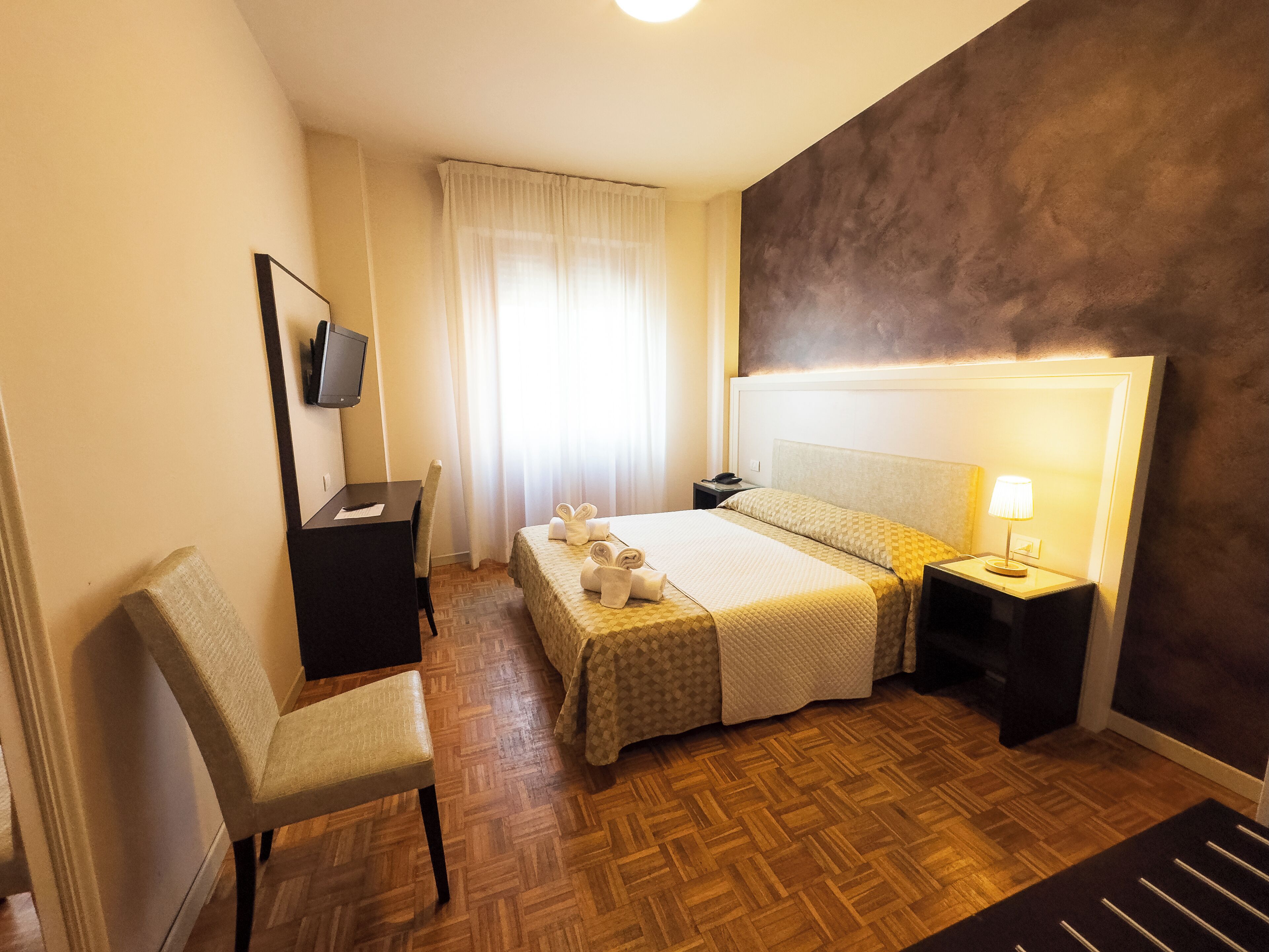 Une chambre d’hôtel avec un lit, une table de chevet, une chaise et un téléviseur fixé au mur.