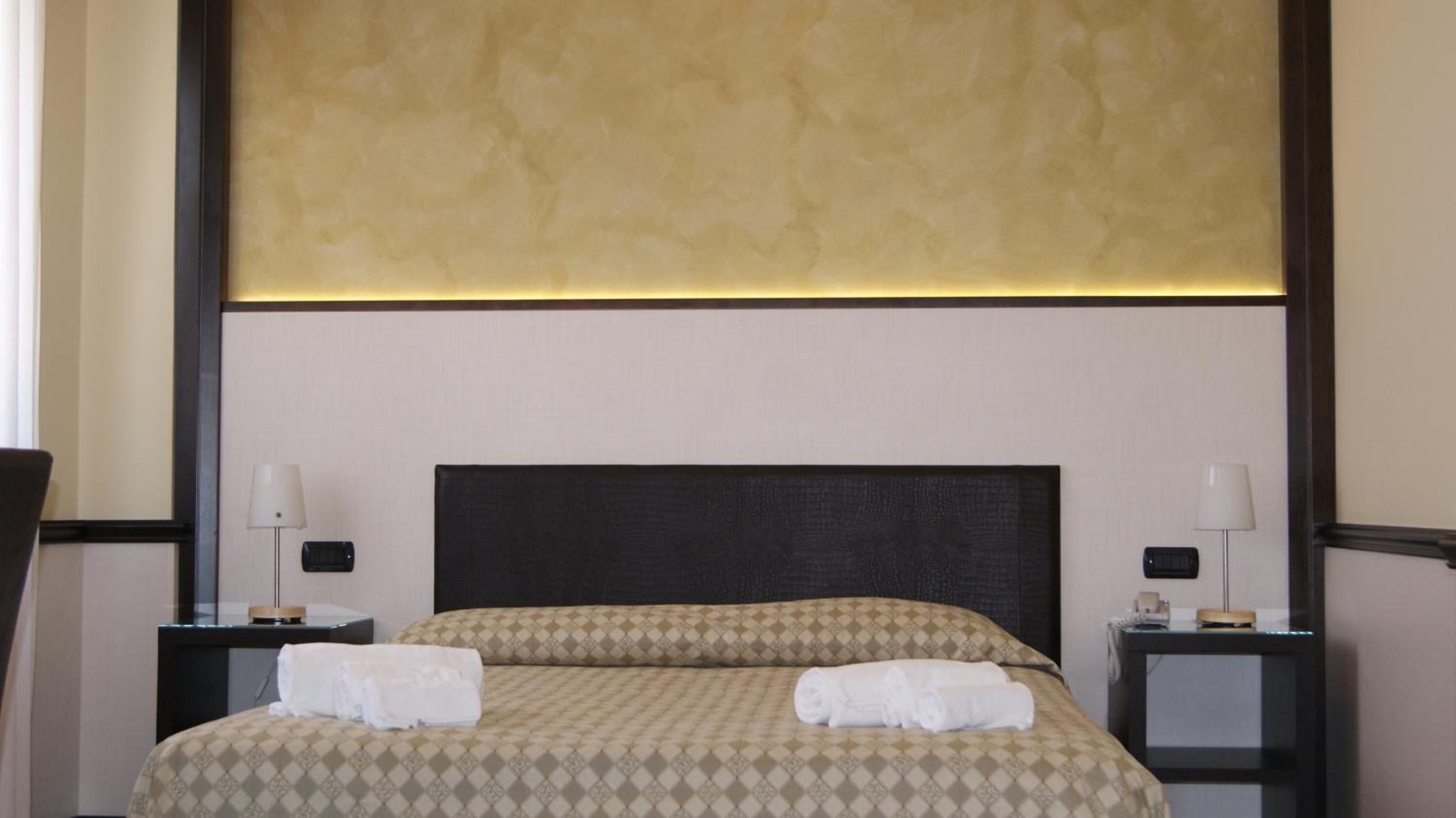 Una camera d'albergo con un letto grande, due comodini e una testiera con pannello strutturato.