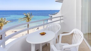 Een balkon met een witte tafel en stoelen, met uitzicht op een strand met palmbomen en de zee.