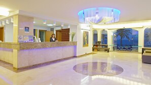 Een hotel receptie met een baliemedewerker, een receptiebalie, een groot rond vloerontwerp en uitzicht op zee door grote ramen.