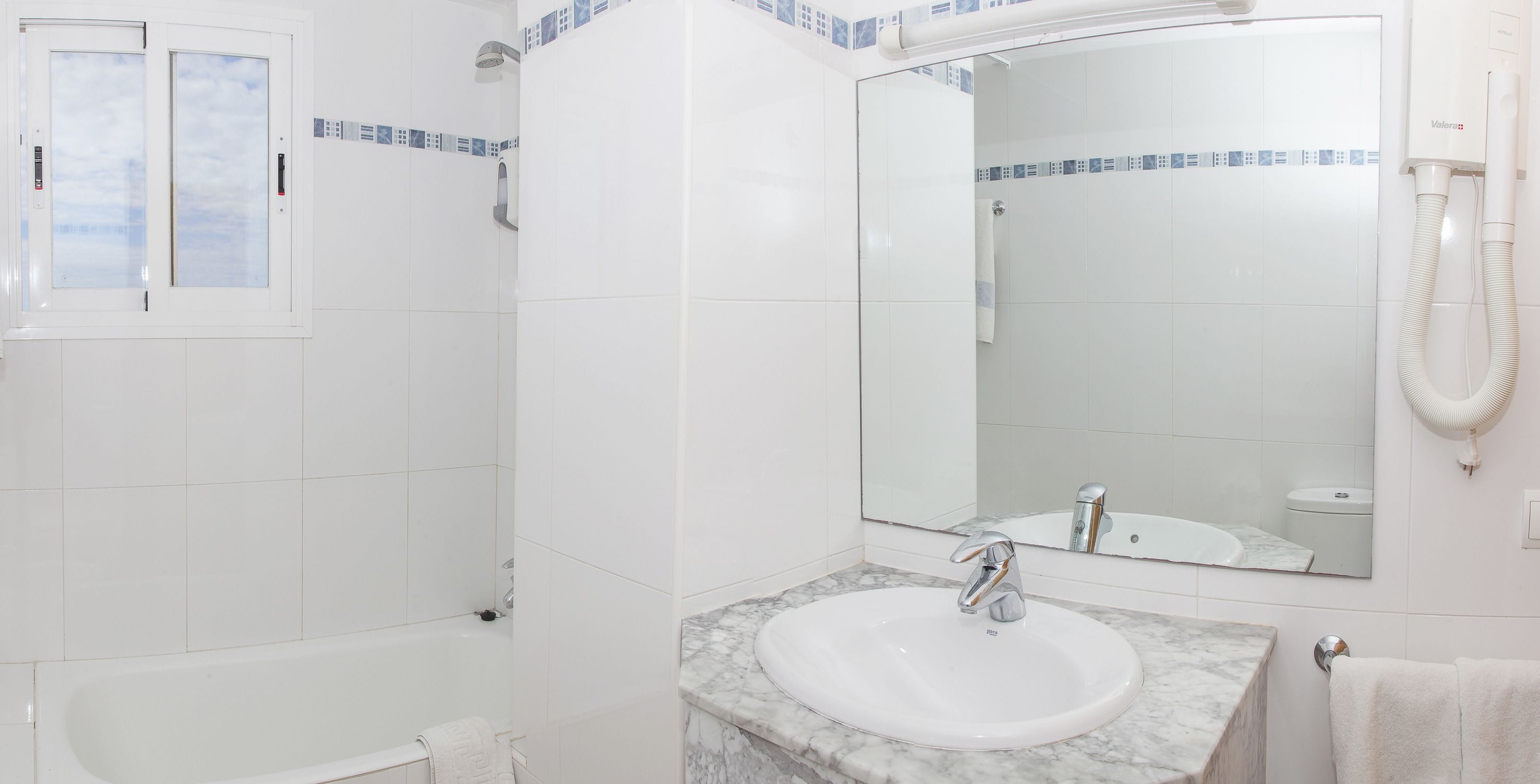 Un baño con bañera, lavabo con encimera de mármol y ducha con puerta de cristal.