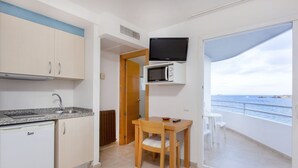 Een functionele keuken met een ingebouwde magnetron, een kleine koelkast, en een eethoek met een tafel en stoelen.