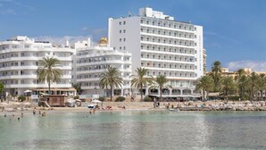 Een kusthotel met meerdere verdiepingen, palmbomen en een strand met boten.