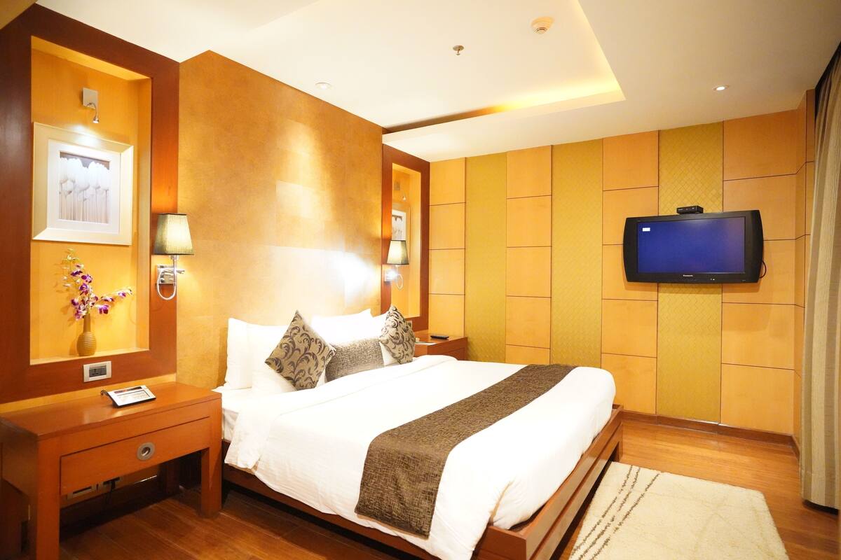 Une chambre d’hôtel avec un grand lit, des tables de chevet, un téléviseur à écran plat fixé au mur et un plancher en bois.