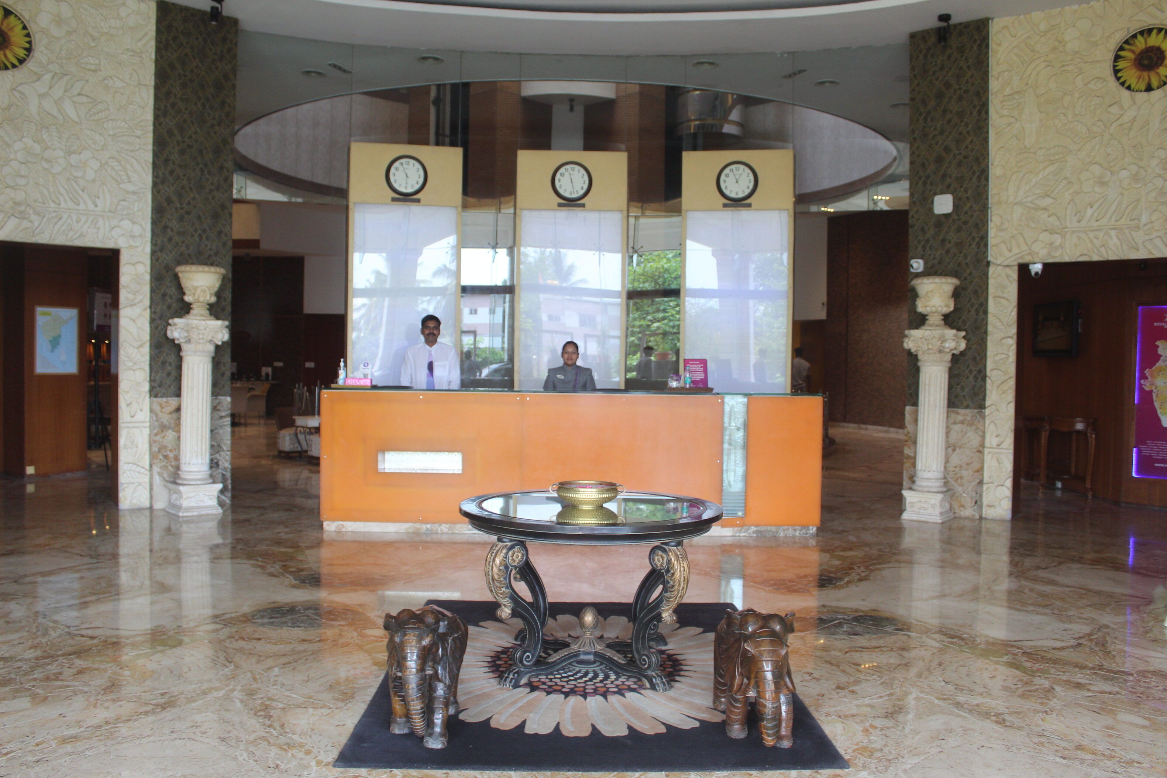 A lobby with a reception desk, three clocks, and a decorative table with a statue.