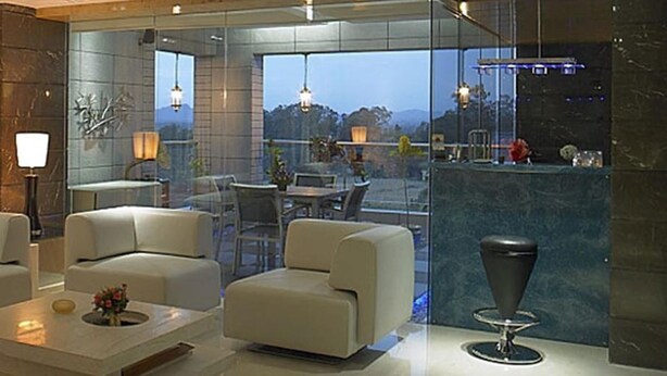 Una sala de estar moderna con un sofá, sillones y una mesa de centro. Se ve un comedor y un balcón con barandilla.