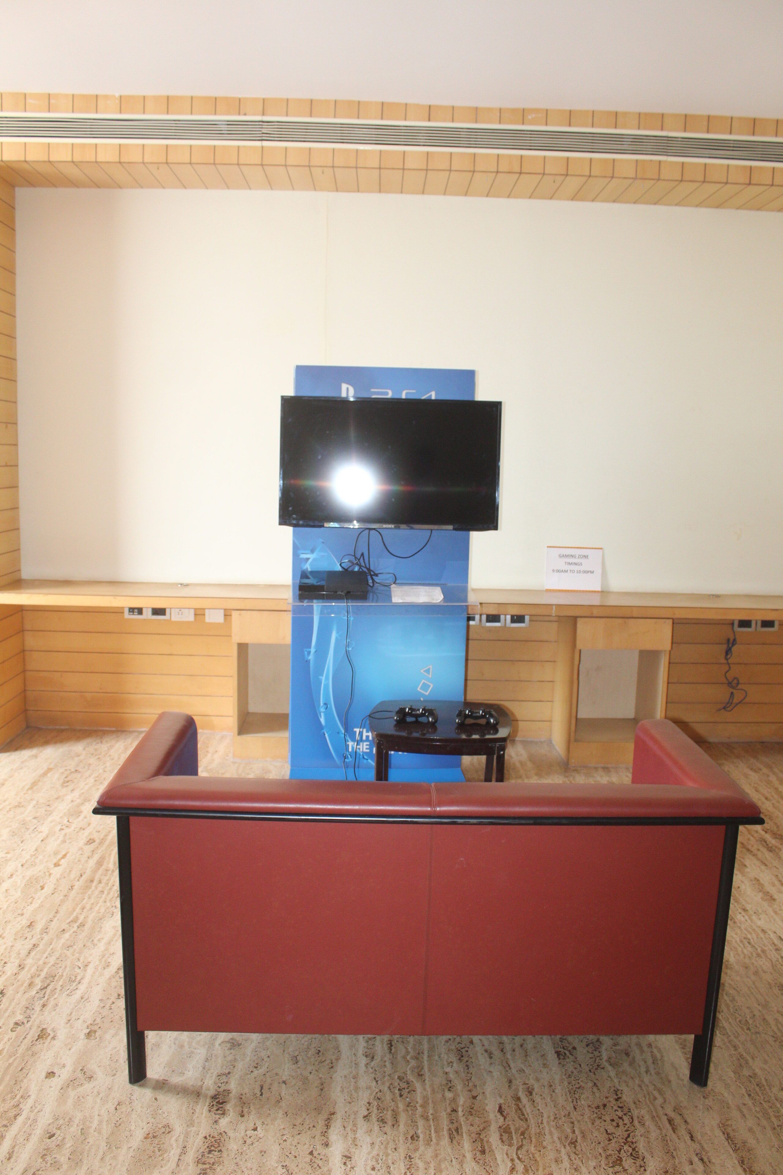 A room with a television mounted on the wall, a wooden desk, and a red couch.