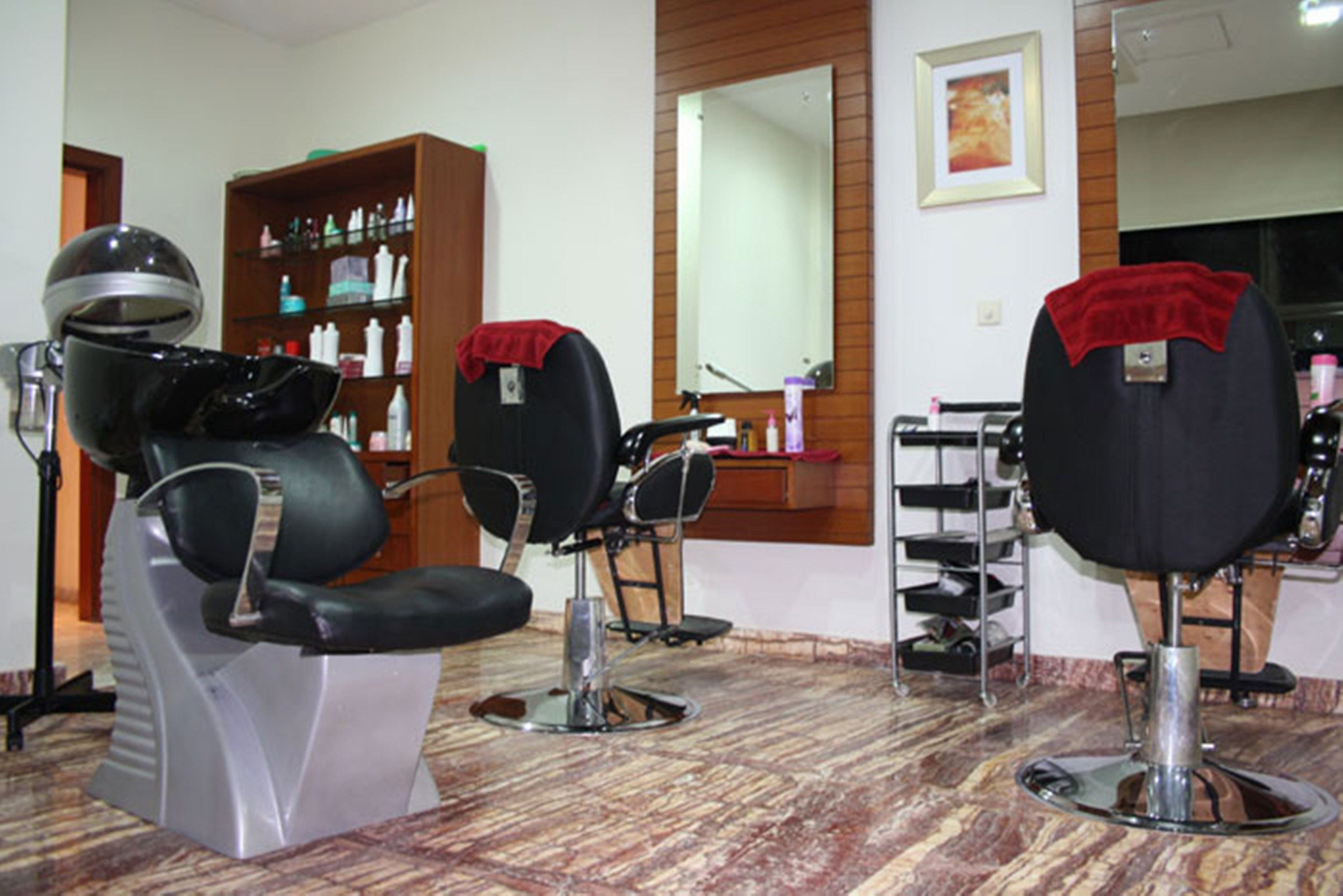 A salon with three black salon chairs, a large mirror, and a shelf with various hair products.