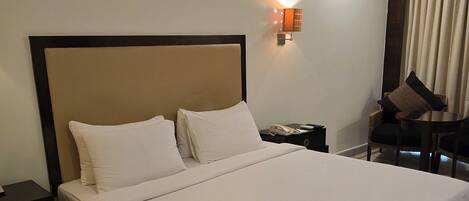 A hotel room with a large bed, a nightstand, a chair, and a wall-mounted lamp.