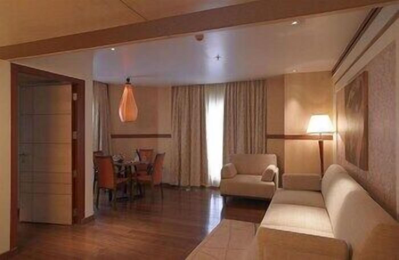 A hotel room with a dining area, a sofa, a lamp, and a door.