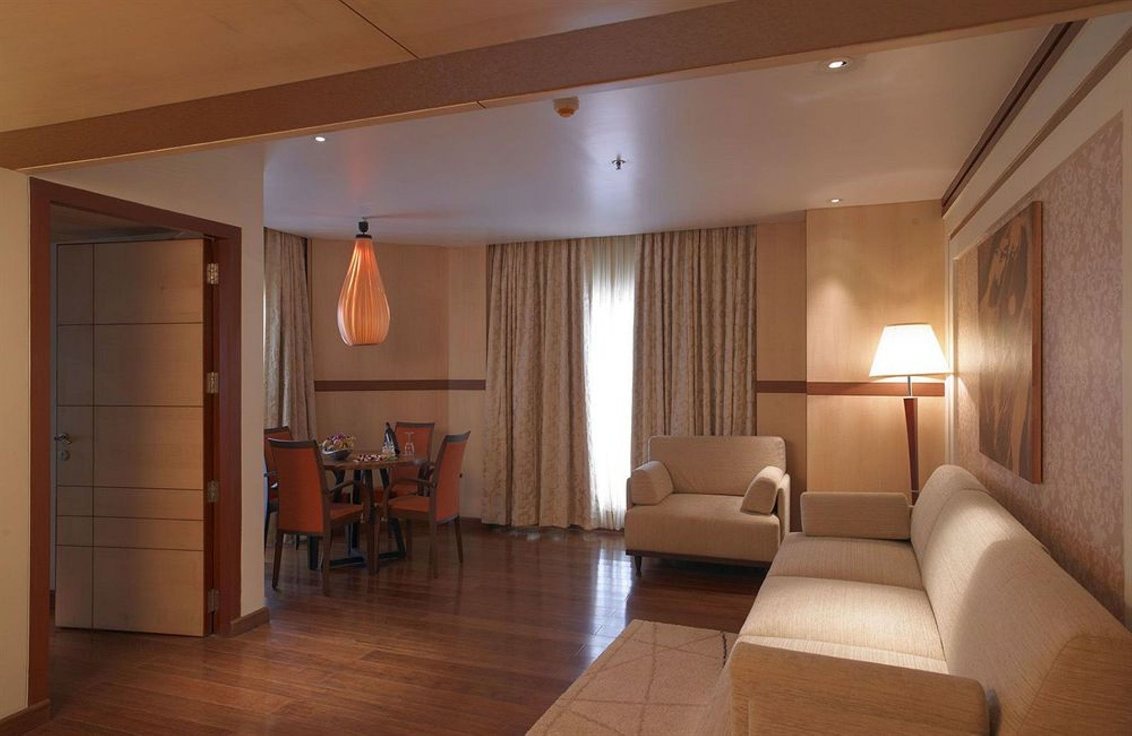A hotel room with a dining area, a sofa, a lamp, and a ceiling light.
