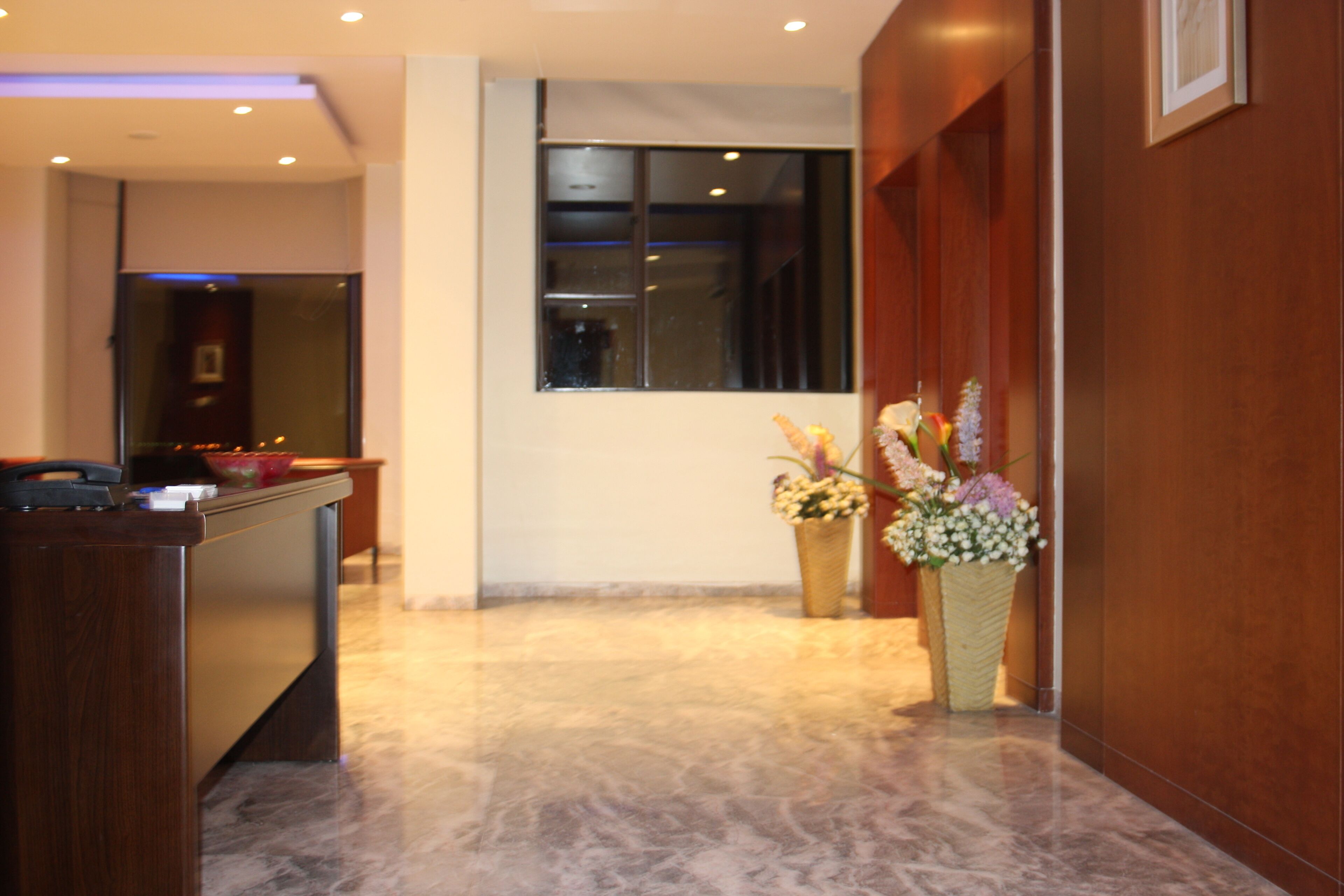 A reception area with a wooden reception desk, a large window, and two flower arrangements on the floor.