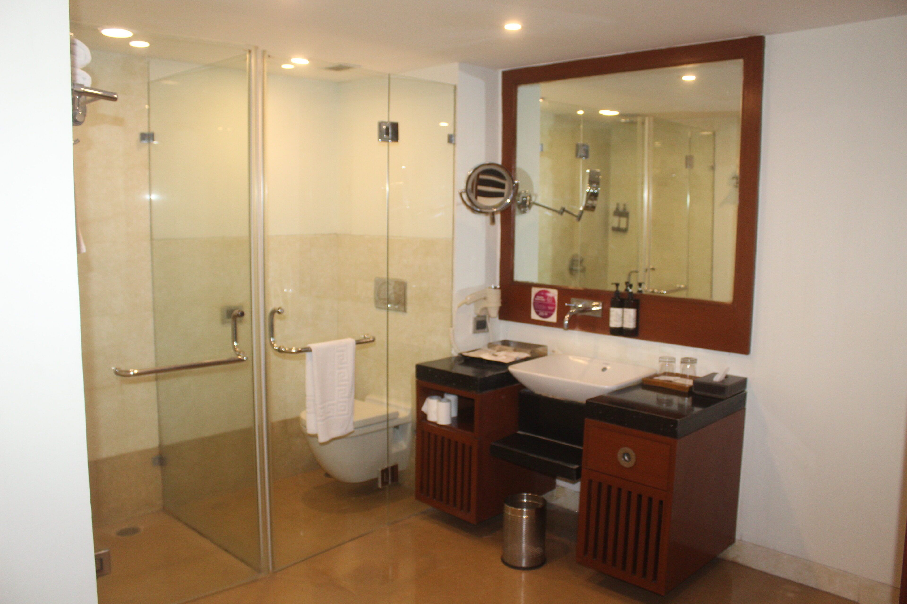 A modern bathroom with a glass-enclosed shower, a white toilet, a sink with a mirror above it, and a trash bin.