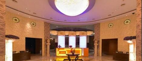 Un hall de hotel con una recepción central, una lámpara circular grande en el techo y suelo de mármol.