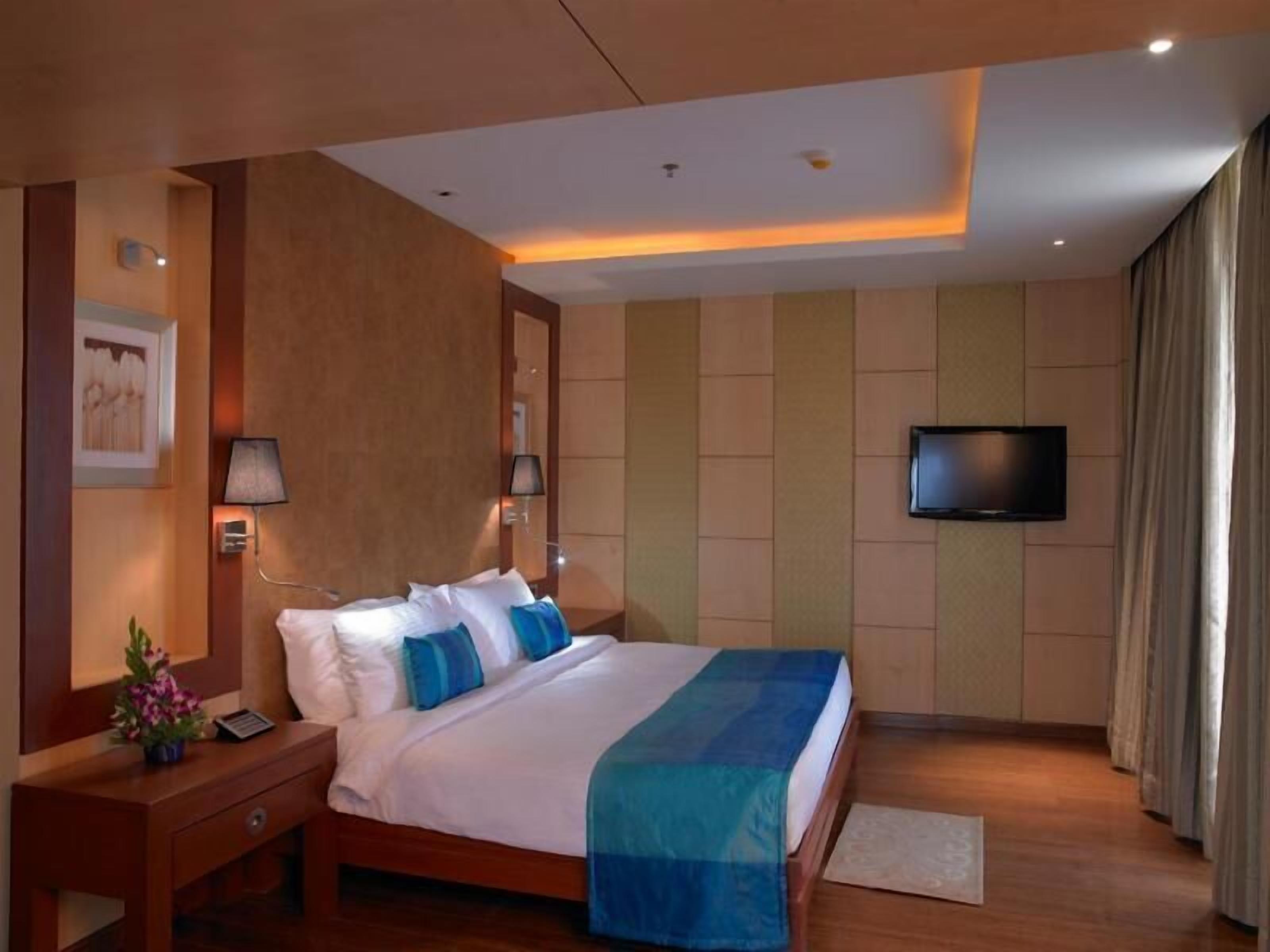A hotel room with a bed, bedside tables, a TV, and a wall-mounted lamp.