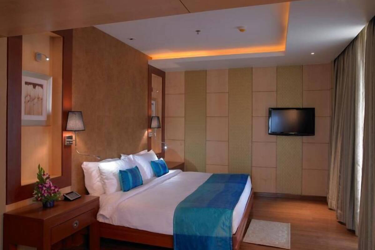 Une chambre d’hôtel équipée d’un lit, de tables de chevet, d’une télévision et d’une lampe fixée au mur.