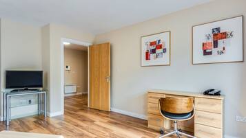 A modern hotel room with a wooden desk, a chair, a television on a glass console, and artwork on the wall.